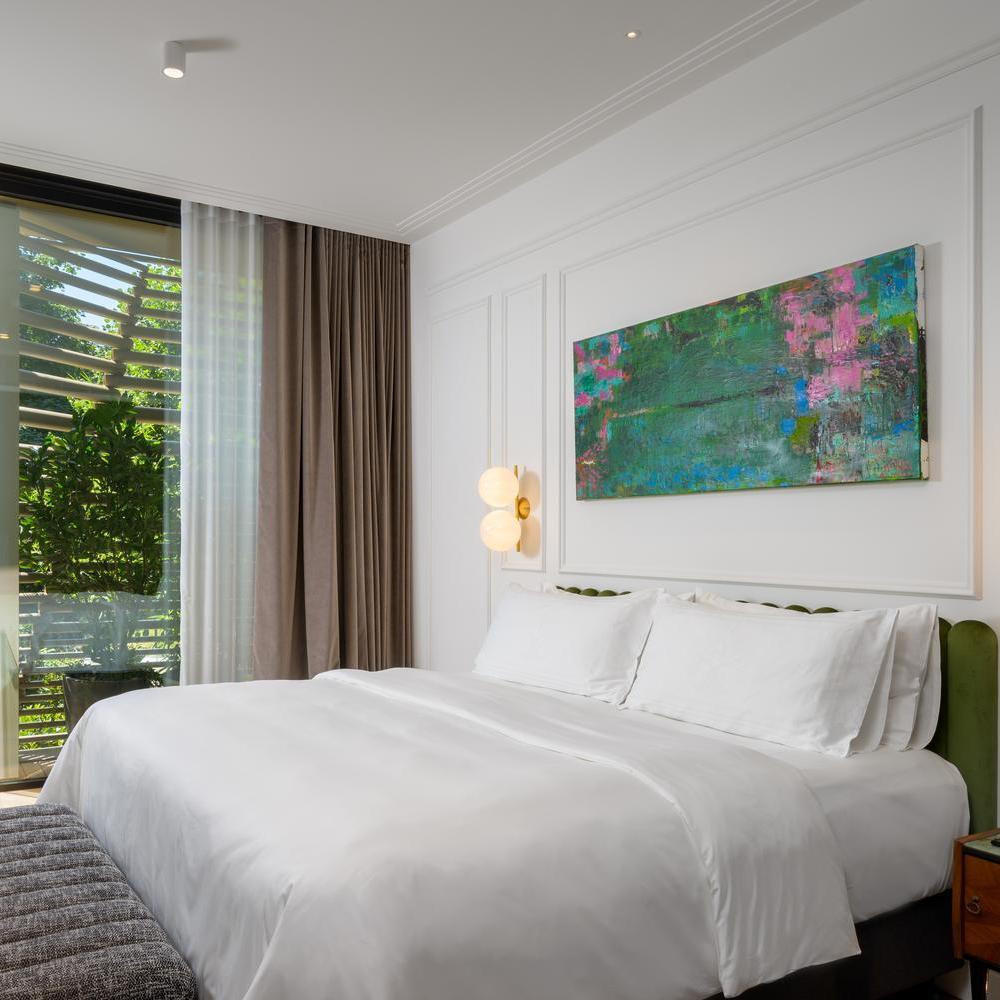 Bright hotel bedroom with white linens, a green headboard, and a large blue and green abstract painting.