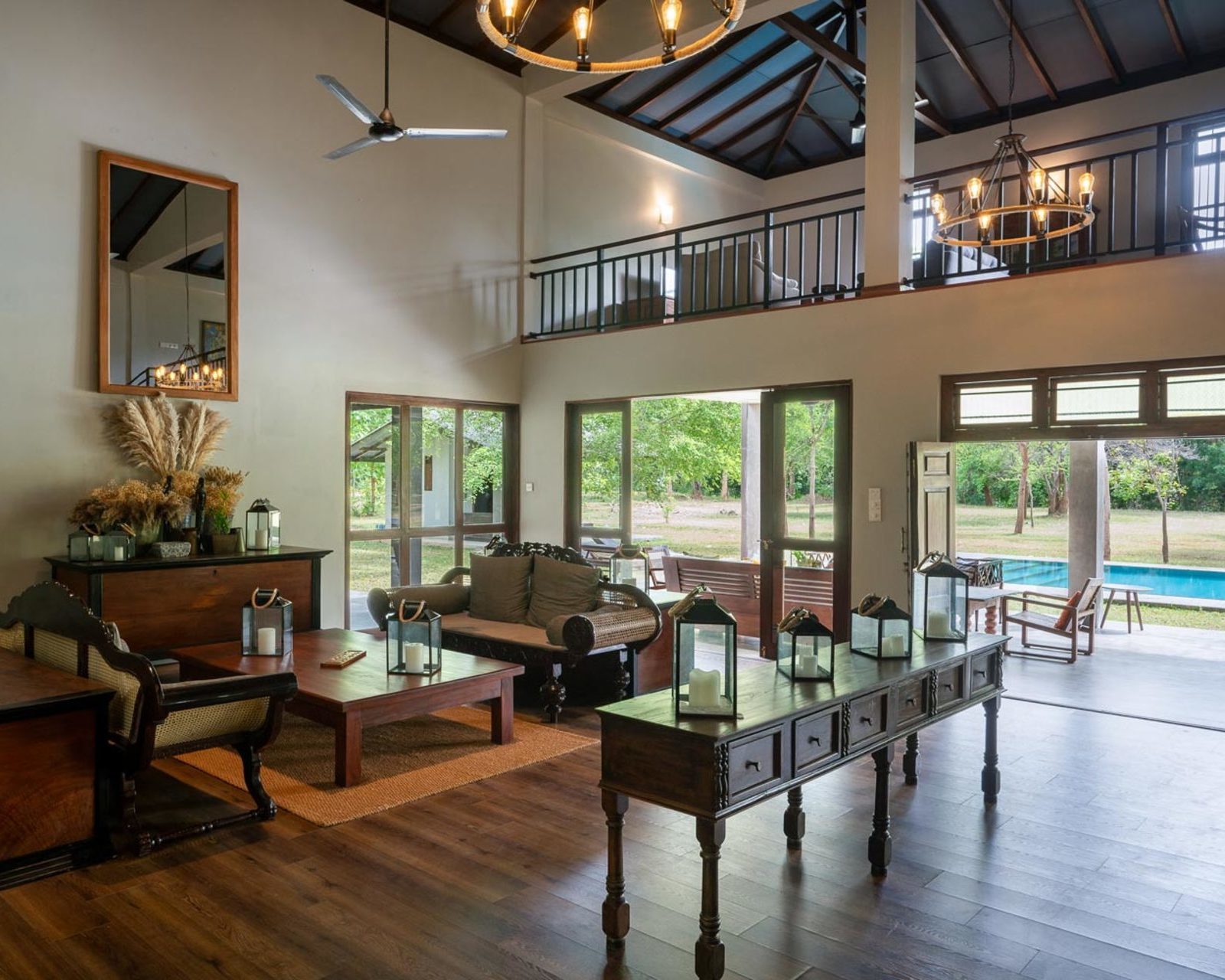 Spacious living area with high ceilings, dark wood furniture, and lanterns leading to an outdoor pool.