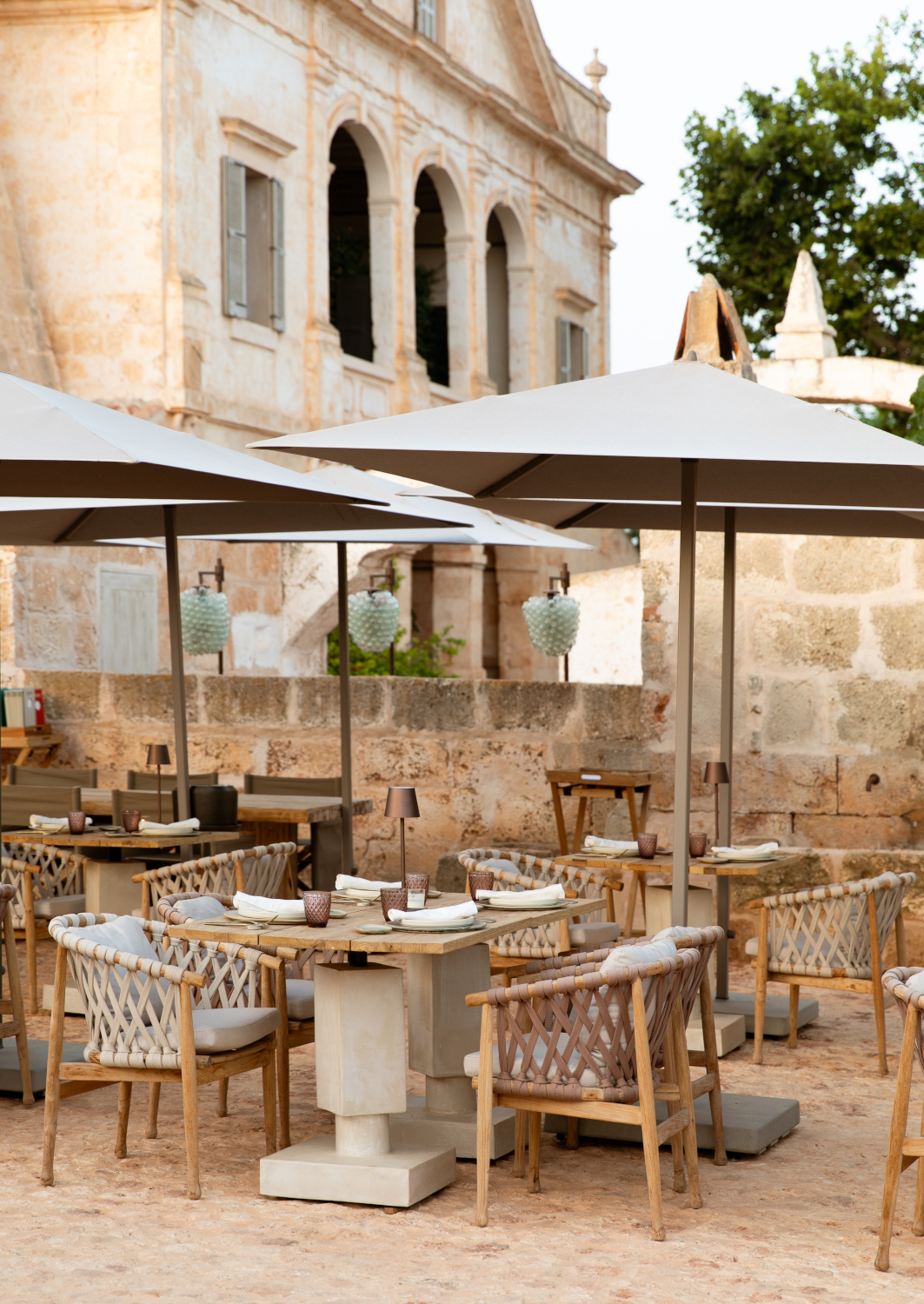 Outdoor dining tables with parasols at Son Vell in Balearic Islands Spain set against a historic stone facade.