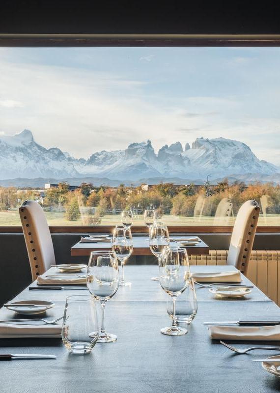 Dining table and chairs with window at the end showing a view of mountains and sky in the background.