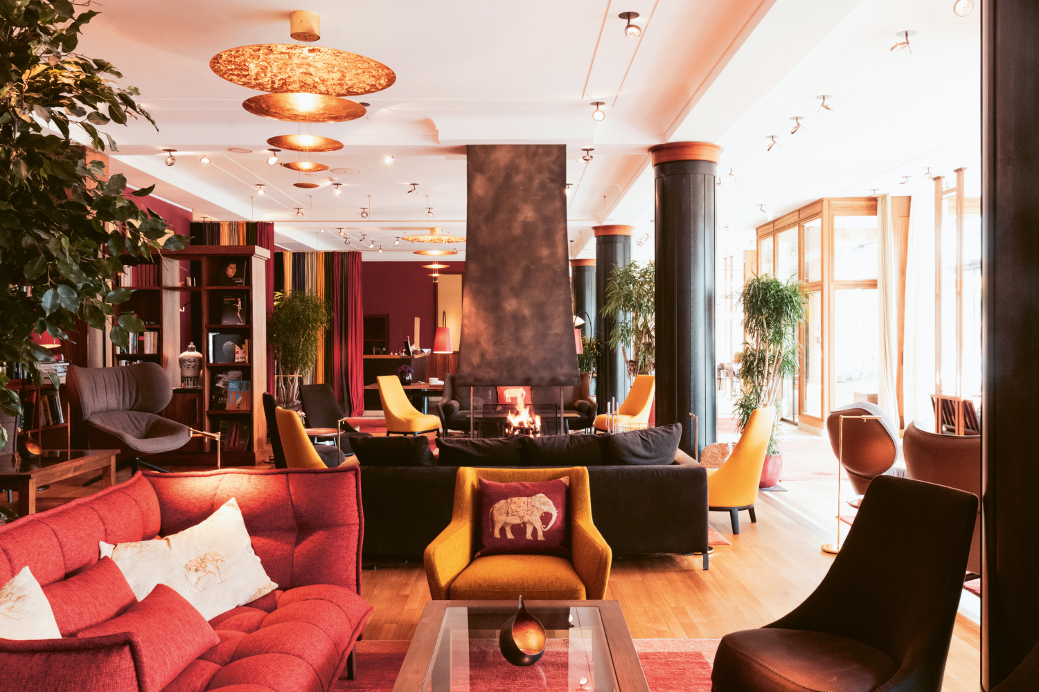 Interior of a hotel lobby with red, brown and black sofas and wood floors, and large black columns down the right-hand side.
