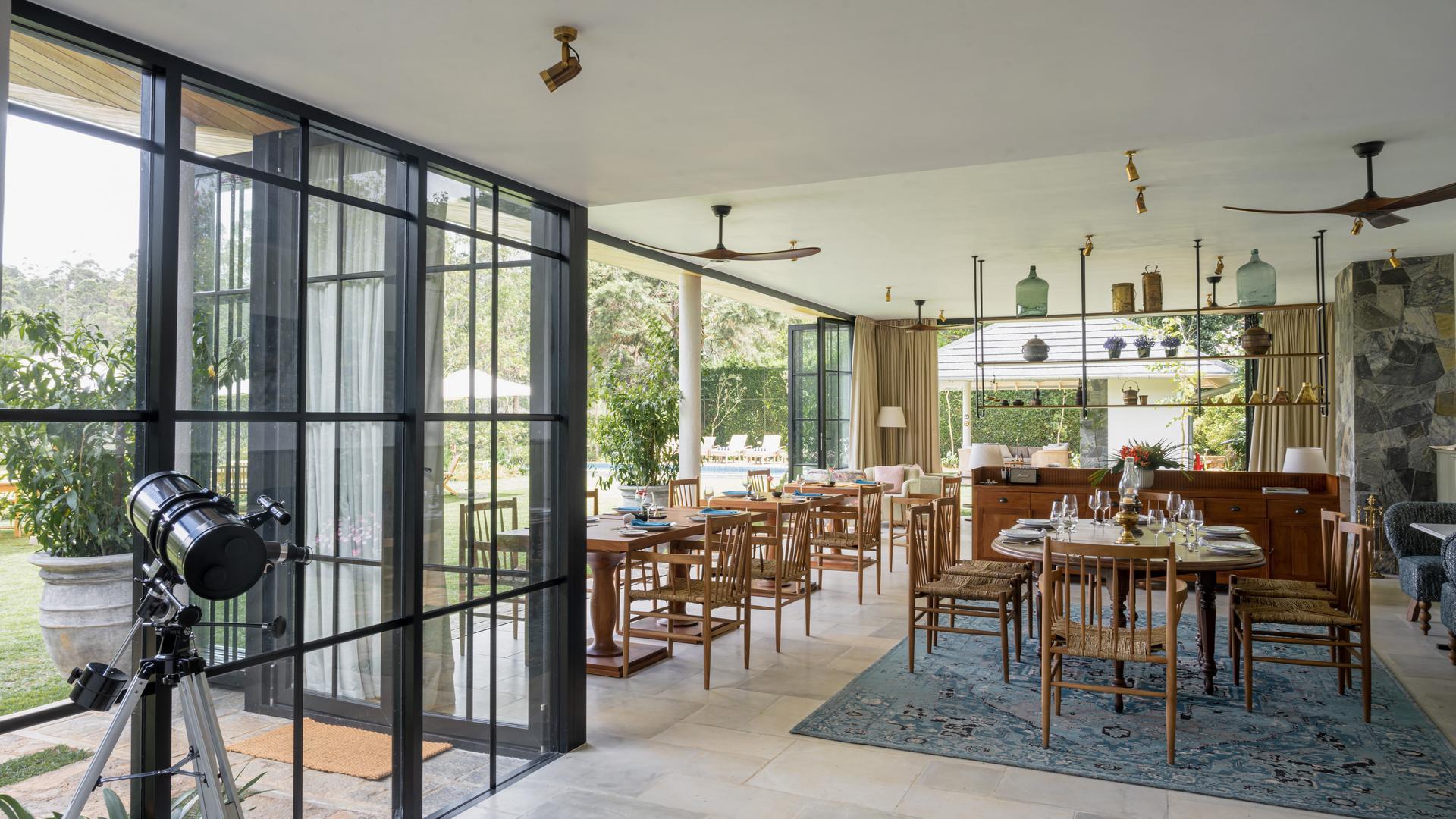 A spacious indoor dining area with floor-to-ceiling windows, wooden tables, and a telescope in the foreground.