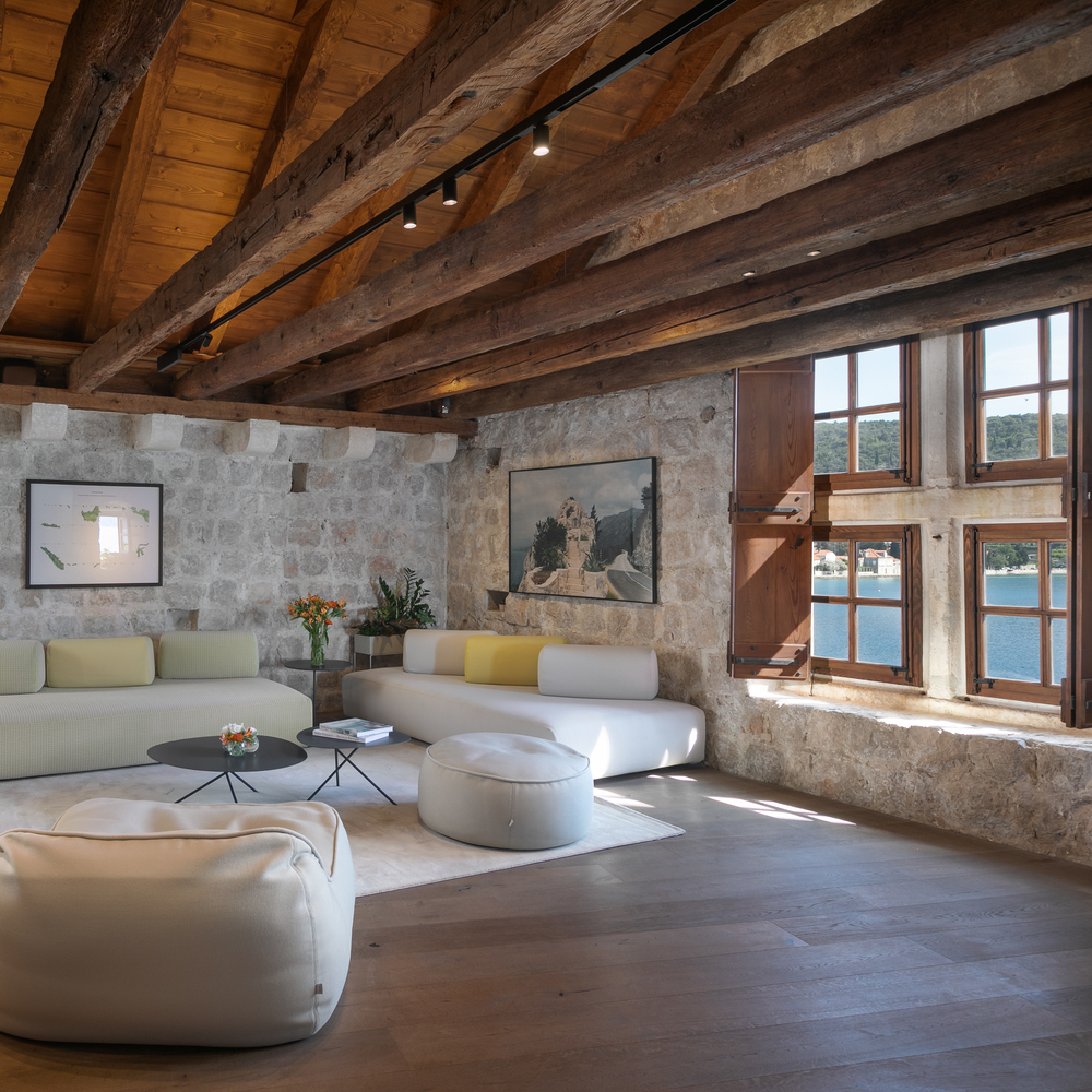 Modern lounge with white sofas and wooden beams in a rustic room with stone walls and a sea view.