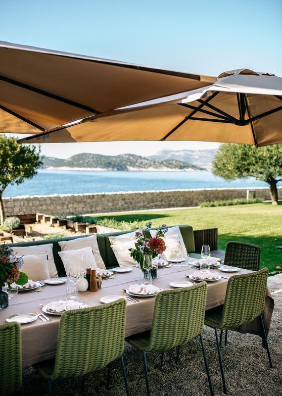 An elegant outdoor dining table set for a meal on a grassy terrace with a view of the sea and islands.