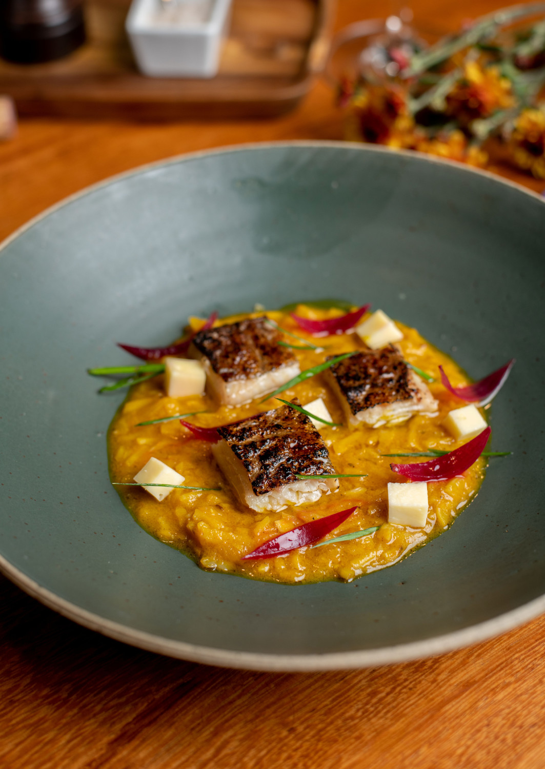 Beautifully plated dish of seared fish with red and green garnishes on a grey ceramic plate.