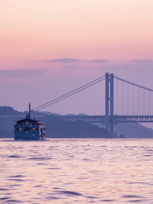 Wide view of the guntû cruise ship at sunset with a bridge in the background