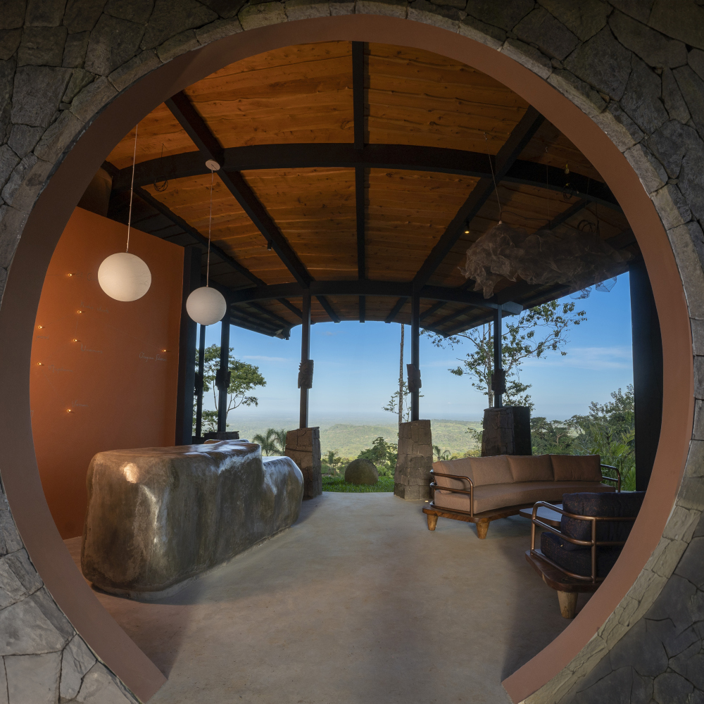 Looking through a round doorway or window in a fisheye lens to an outdoor terrace overlooking the rainforest canopy and blue sky.