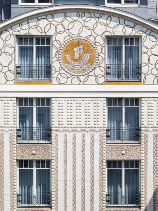 A white building facade with mosaic patterns and an image of a ship at sea