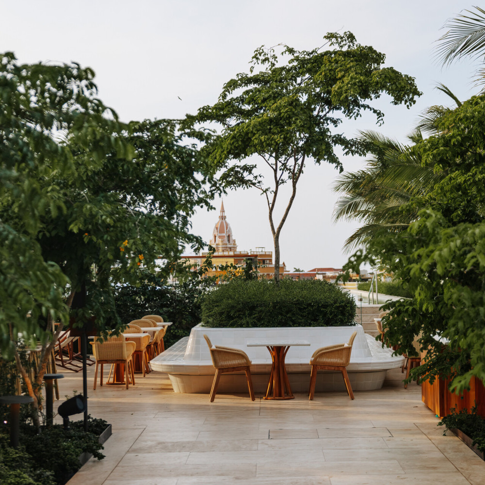 Outdoor dining area with tables scattered around a marble terrace interspersed with greenery and trees and a view of Cartagena's old city beyond.