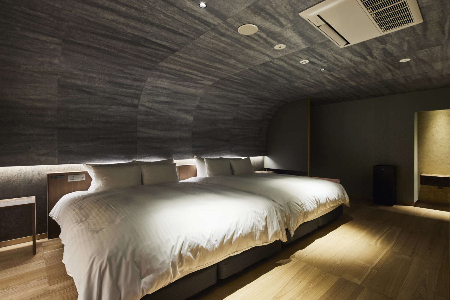 Interior of a double room with two beds with white bedding and rounded stucco ceiling and wood floors.
