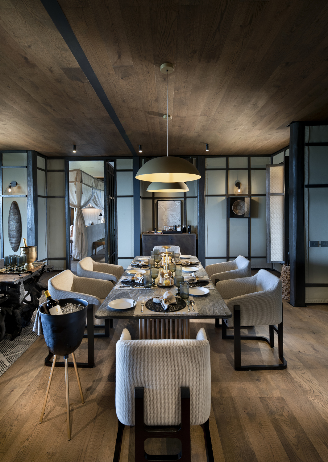 Interior shot of a dining table set for dinner with five grey chairs and two low-hanging lamps above.