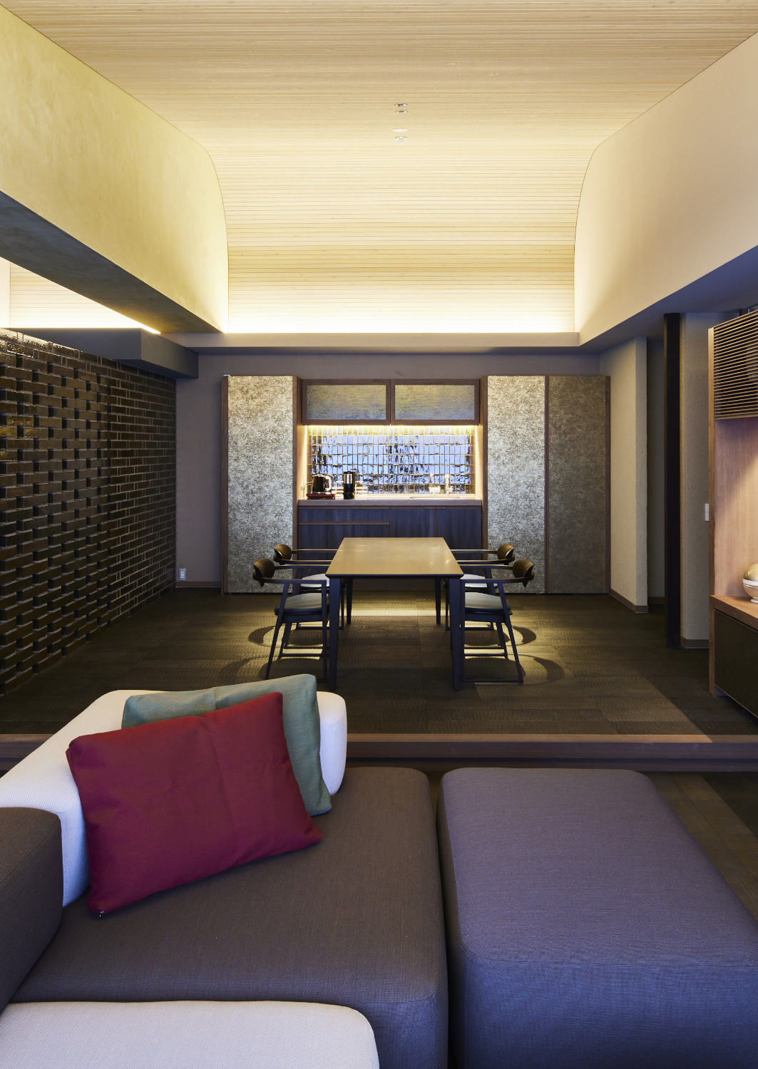 Interior view of a suite's living area with low grey and brown sofas in the foreground and a minimalist table in the background.