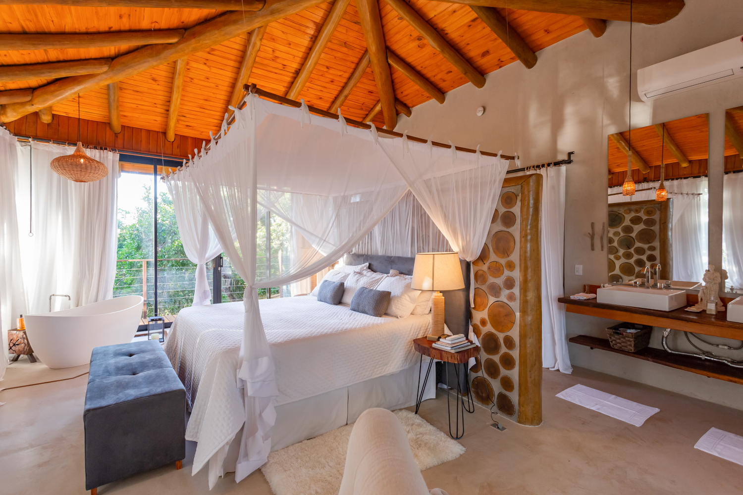 Bonito Villa bedroom with canopy bed with white bedding, a pitched wooden ceiling and large glass doors opening beyond the bed.