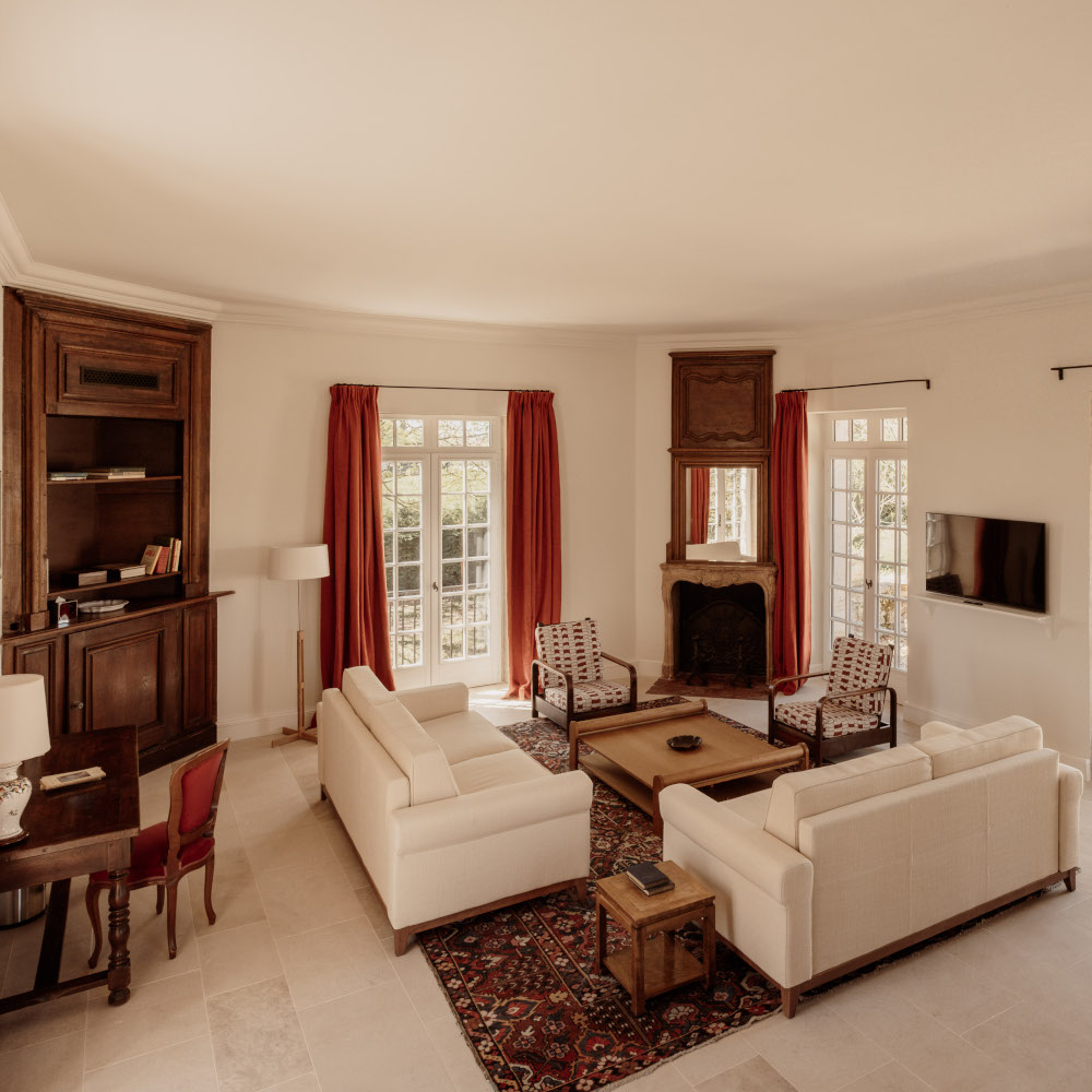 Interior of a living area with white sofas and chairs around a coffee table, a Persian rug and red curtains.