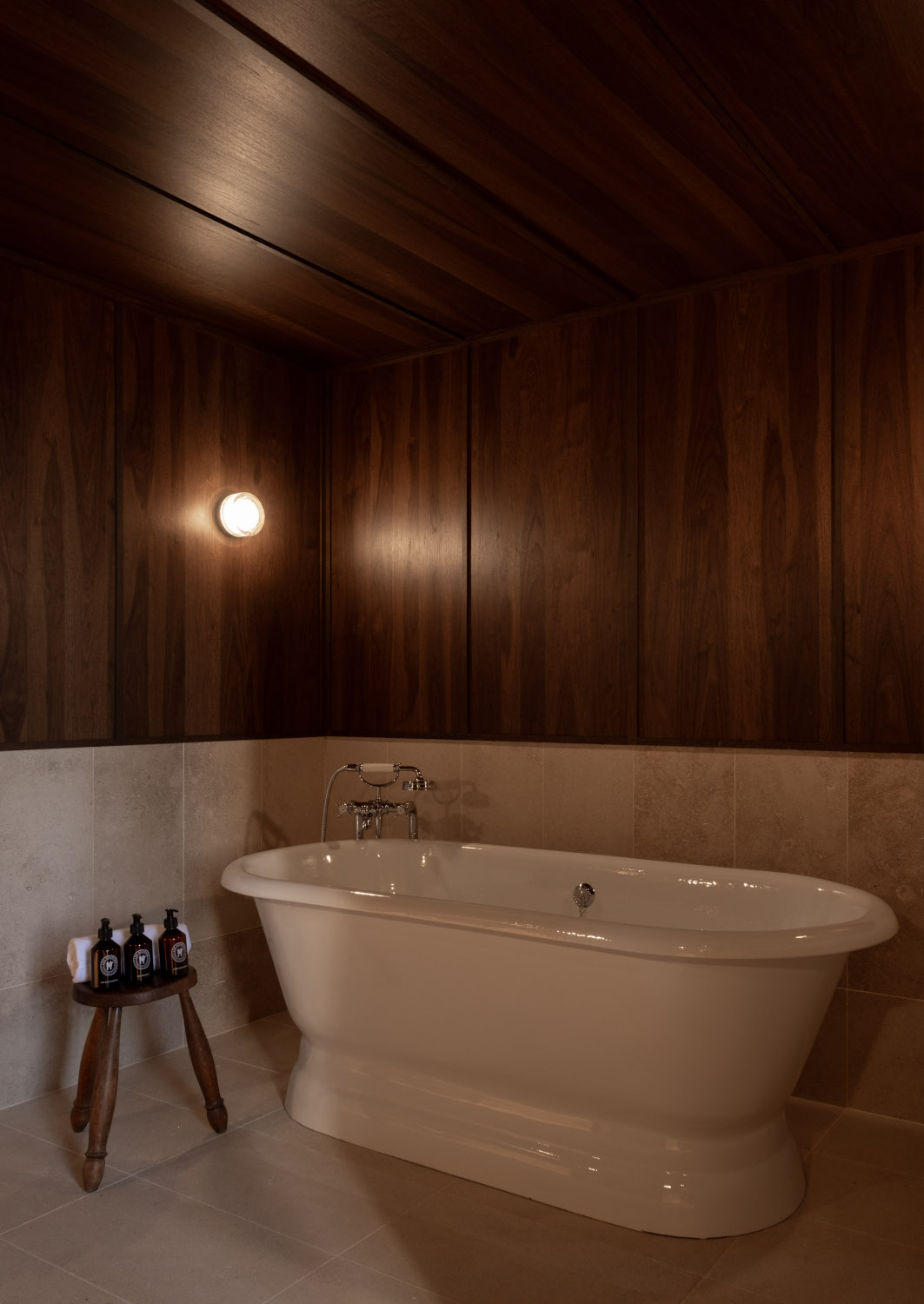 Interior of a bathroom with a standalone white bathtub and dark wood walls.