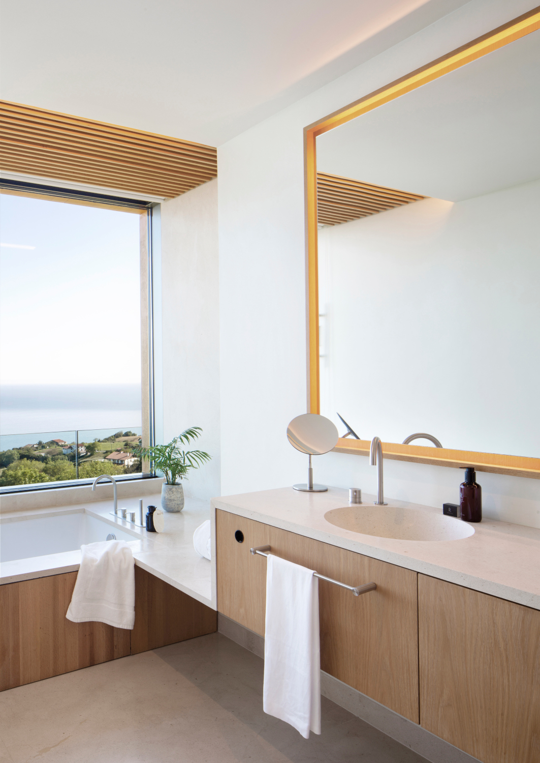 Interior of a minimalist bathroom with a single sink and bathtub and huge window overlooking the sea.