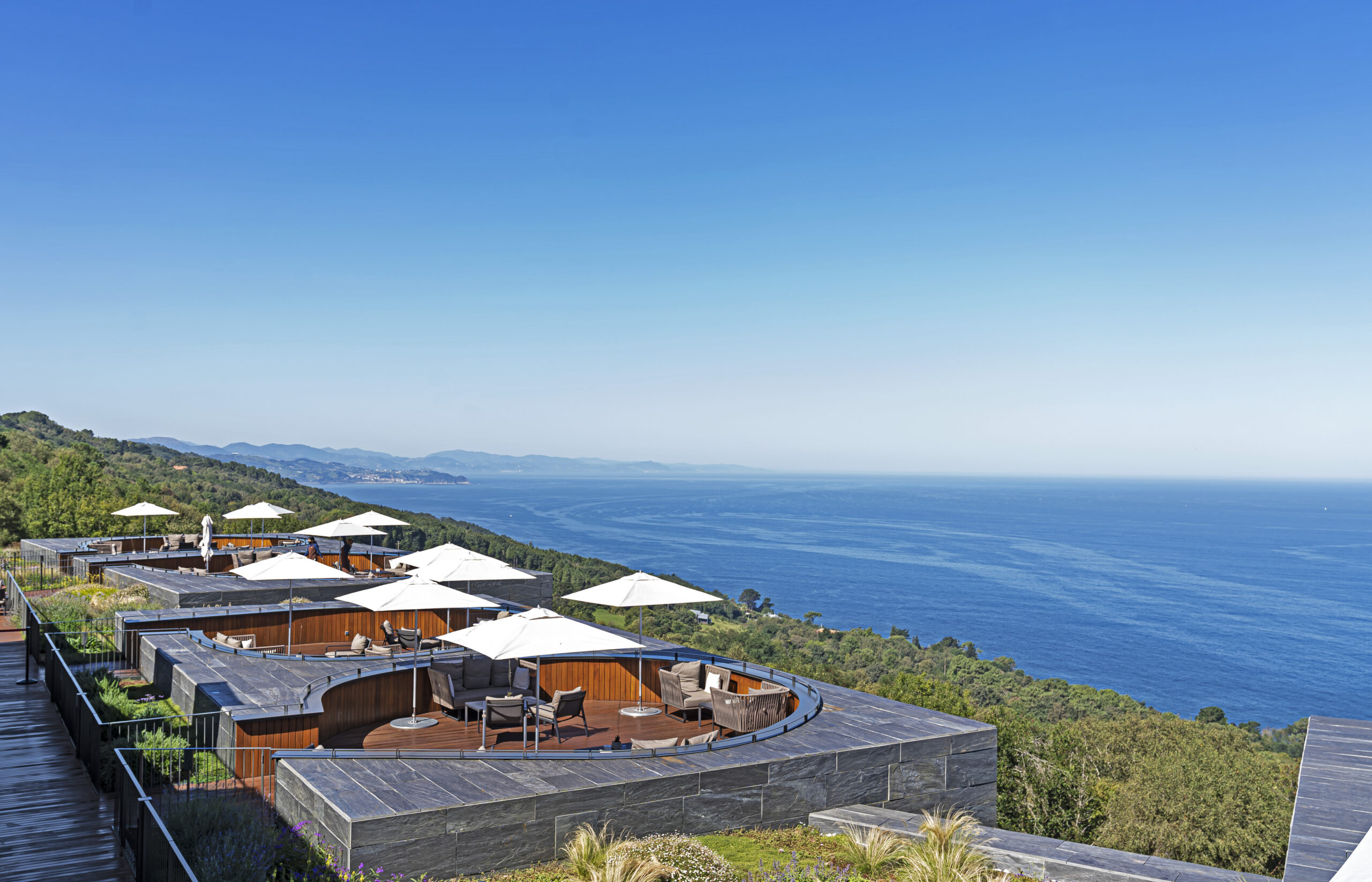 Outdoor terraces at with white umbrellas overlooking a vast blue sea.