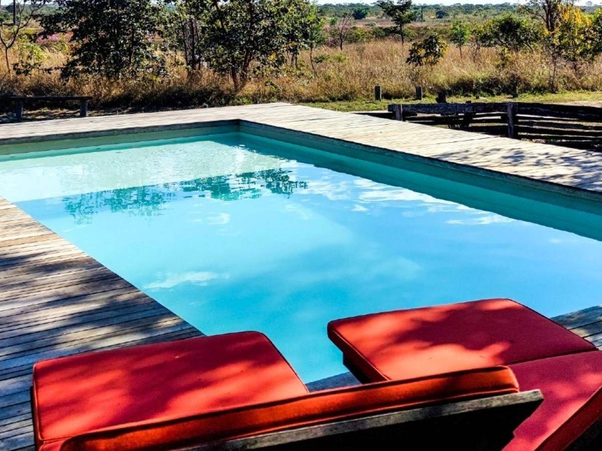 Two red sun loungers in the foreground and a medium-sized outdoor pool surrounded by a wooden deck with views of the Cerrado wilderness.