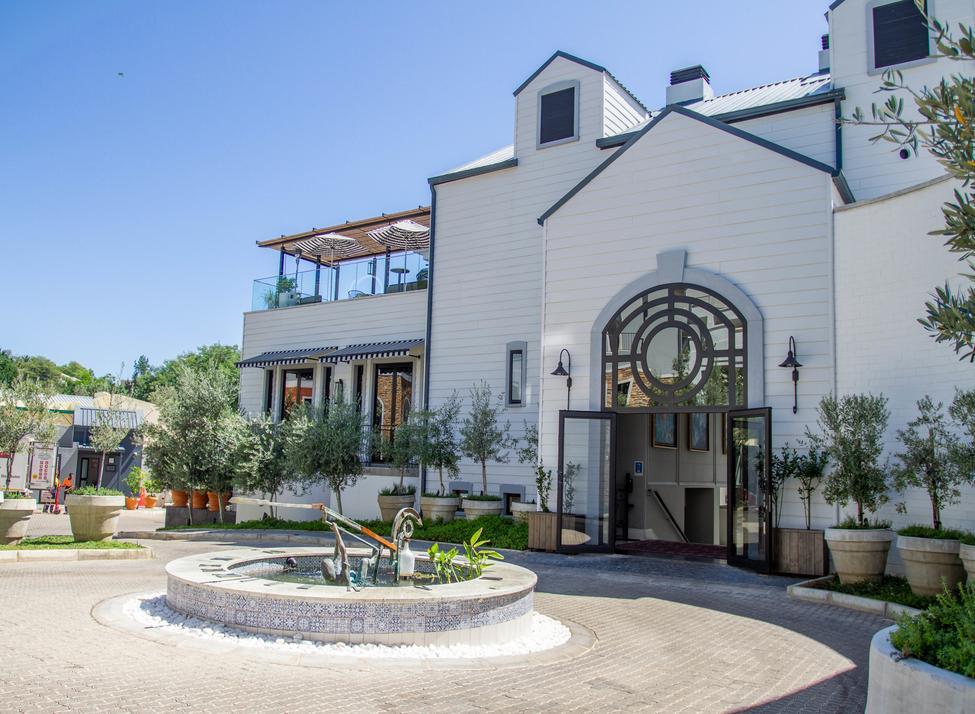 A white-painted timber building with black-framed windows and glass doors, opening to a courtyard with water features and plants.