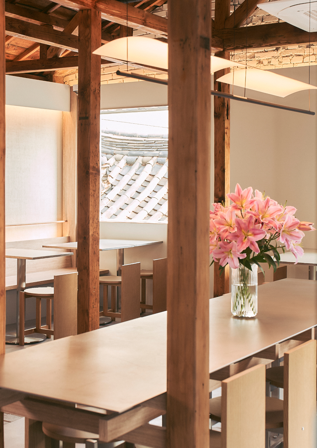 Interior of a cafe in a traditional Korean hanok house hotel with exposed beams, white walls and a pink floral arrangement in a vase on the counter.