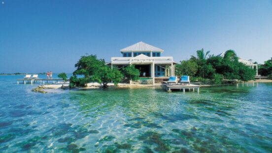 A white beach house on a private tropical island with turquoise water and a wooden pier.