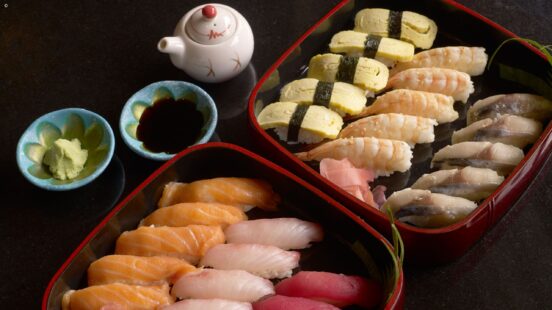 A close-up of two trays filled with various types of nigiri sushi, ginger, and wasabi.