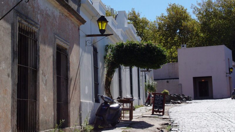 Narrow cobblestone road with a parked motor scooter, yellow street lamp, and colonial-style architecture.