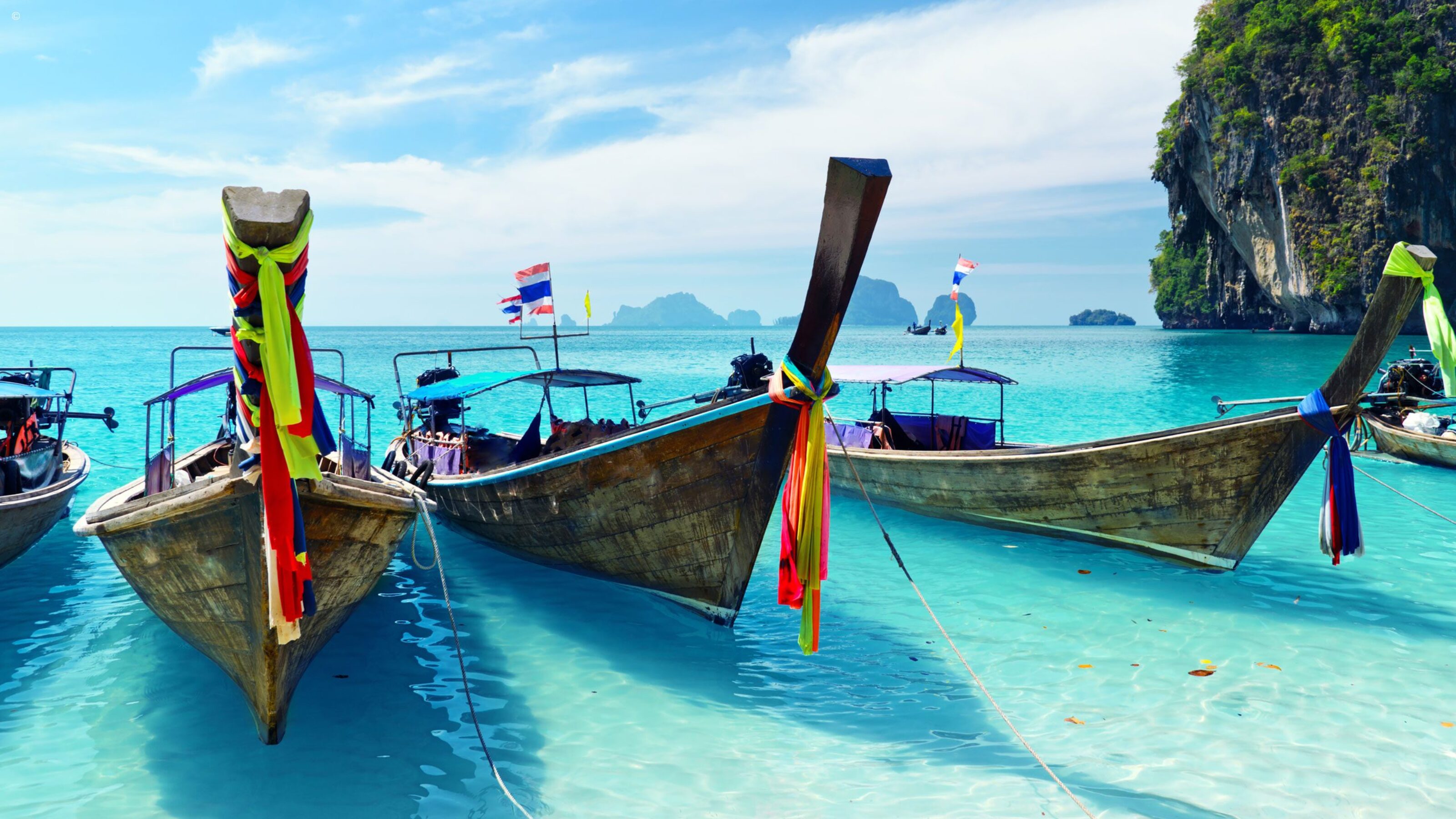Traditional longtail boats with colorful ribbons rest in crystal clear shallow water for luxury Asia honeymoons.