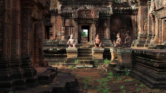 Intricate reddish sandstone carvings and statues of guardians decorate the central sanctuary of the Banteay Srei temple.