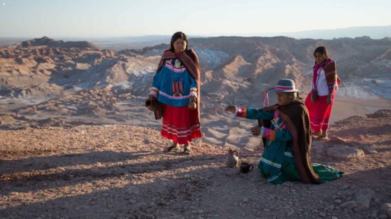 People in colorful traditional textiles and hats on a rocky ridge with a vast mountain landscape background.