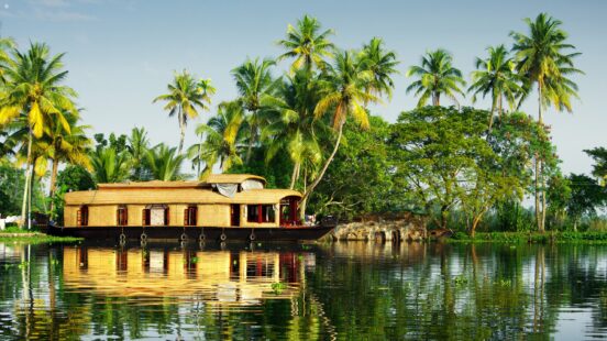 A traditional houseboat on still waters with palm trees behind in Kerala, India