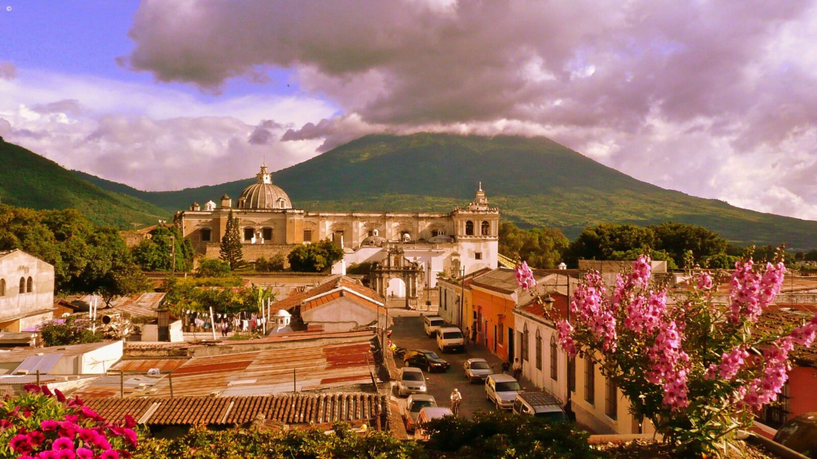 Aerial view of the city of Antigua in Guatemala, framed by pink spring flowers and dramatic mountains
