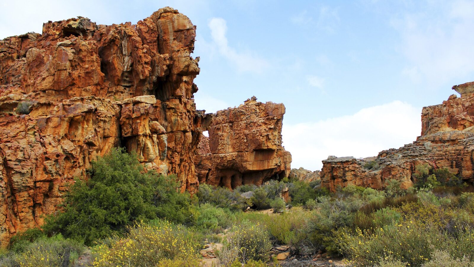Rugged orange rock formations and green bushes under a blue sky during luxury Western Cape tours.