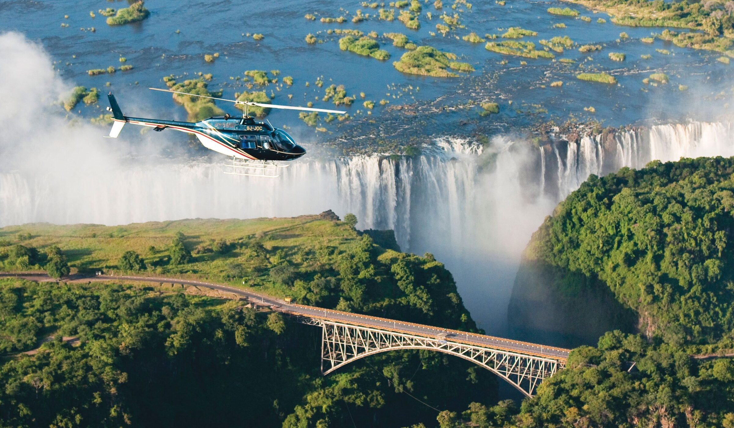 A helicopter soaring over Victoria Falls and the Victoria Falls Bridge during luxury Zambia holidays.