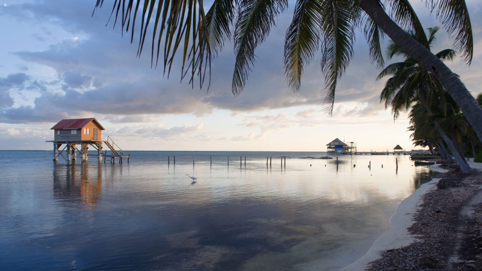 A wooden stilt house over calm water at sunset during luxury Belize tours.