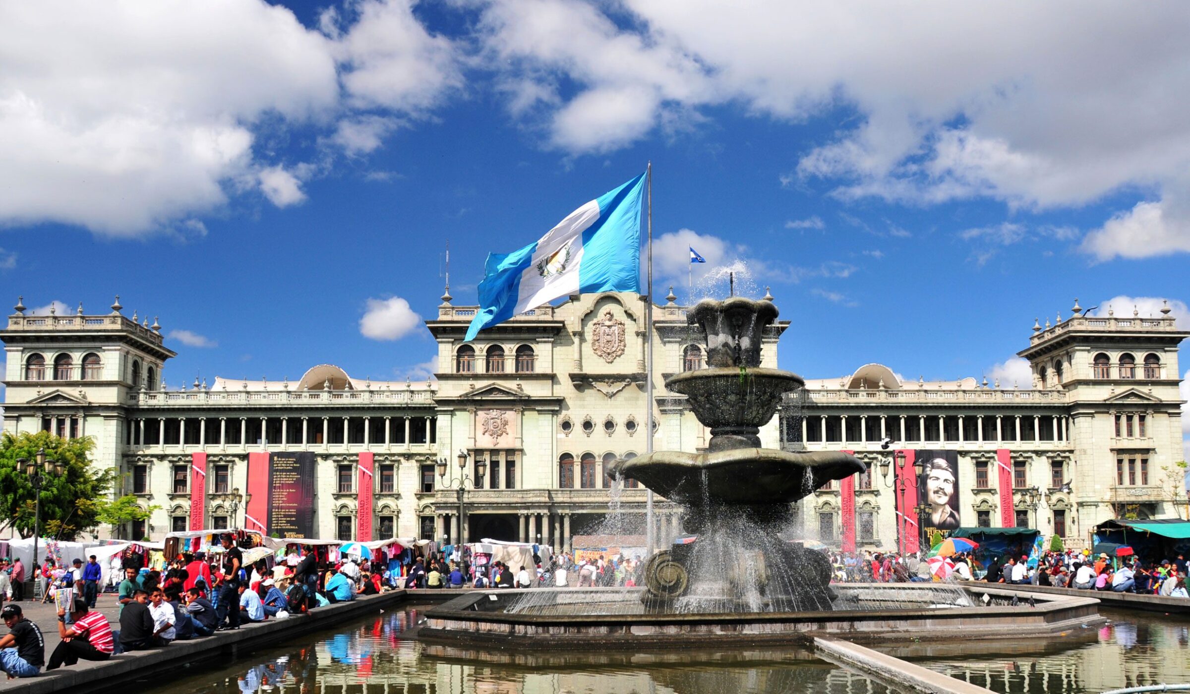 The fountain of Constitution Plaza lined with locals on a sunny day, Guatemala City in Guatemala