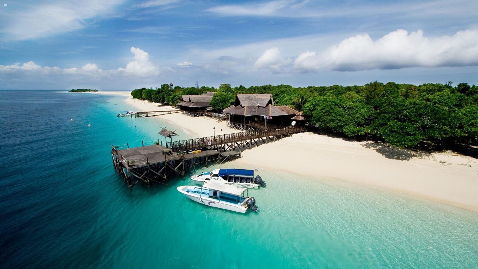 Tropical island beach with a wooden pier and boats available on luxury Borneo vacations.