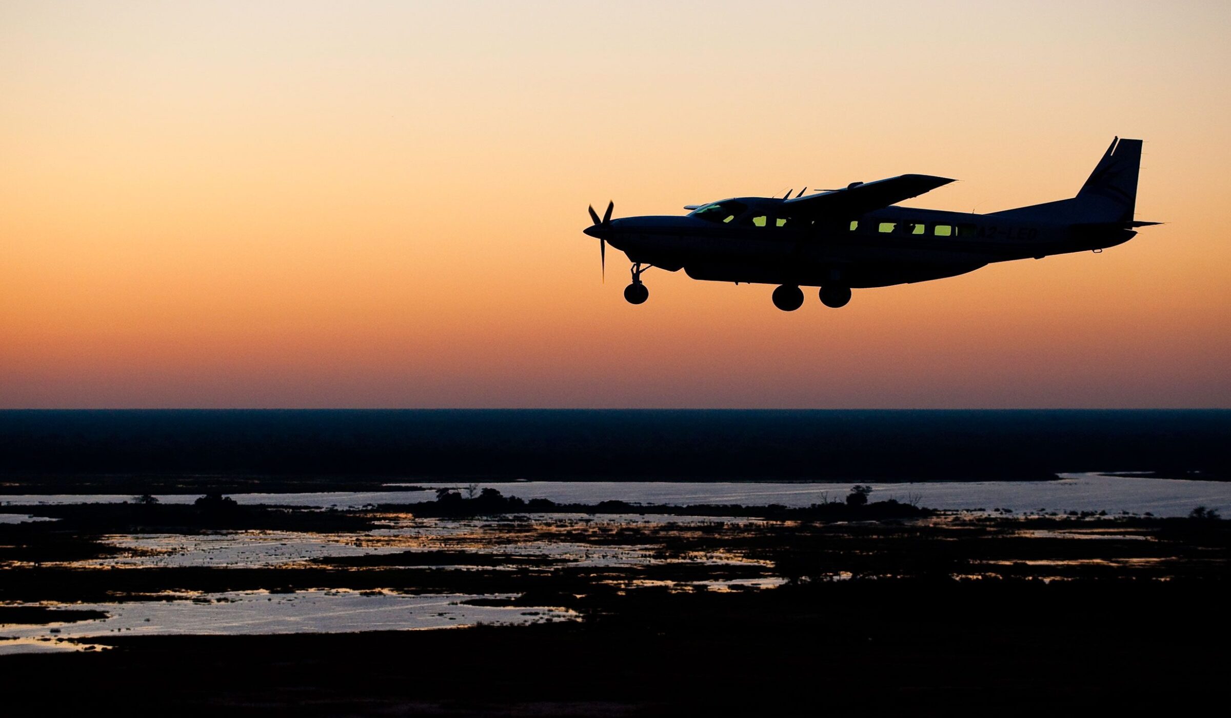 Silhouette of a bush plane flying over a delta at sunset on a Grand Tours of Africa journey.