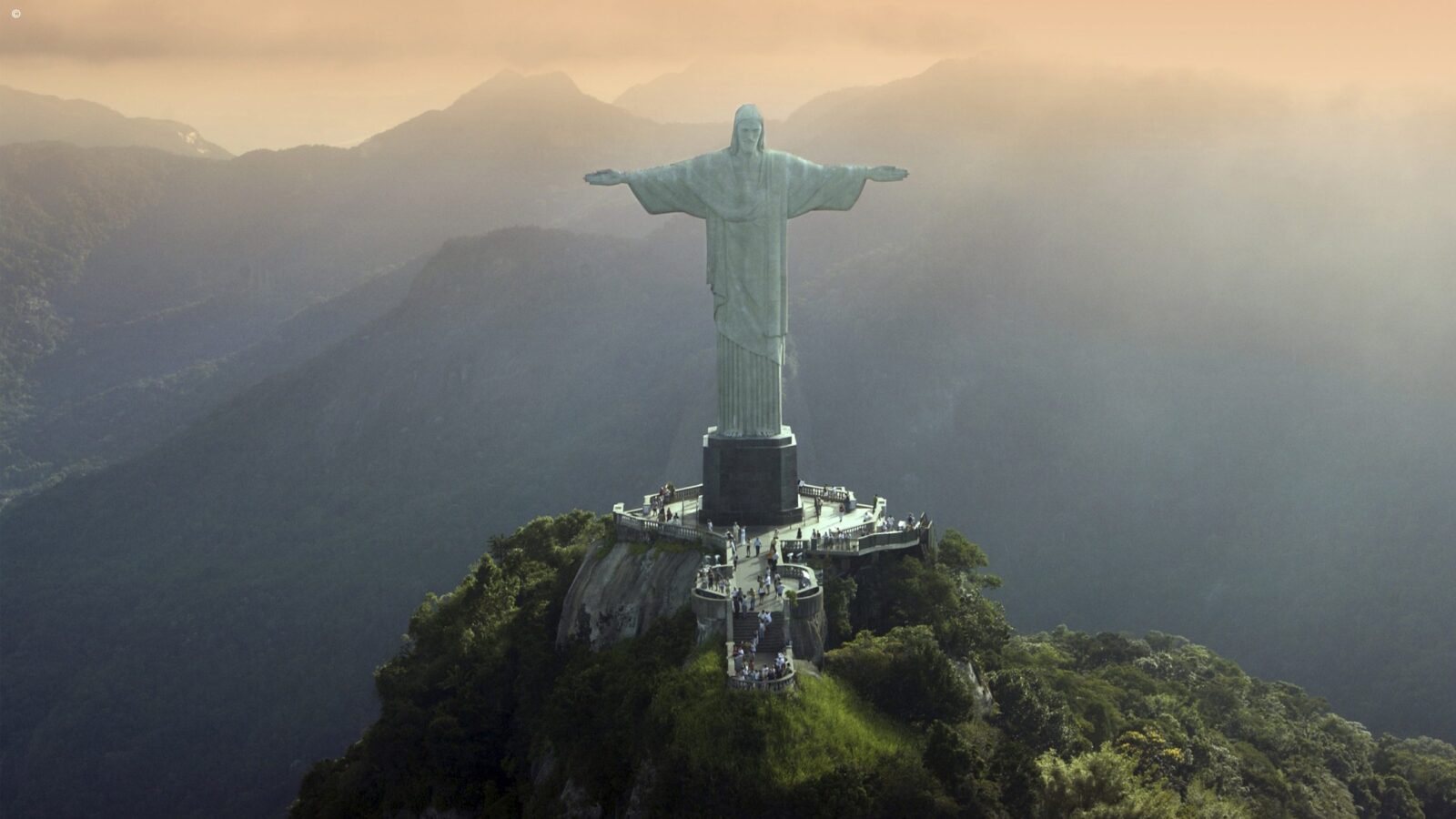 Aerial view of the Christ the Redeemer statue on Mount Corcovado, surrounded by lush, misty mountains at sunset, luxury Latin America grand tour.
