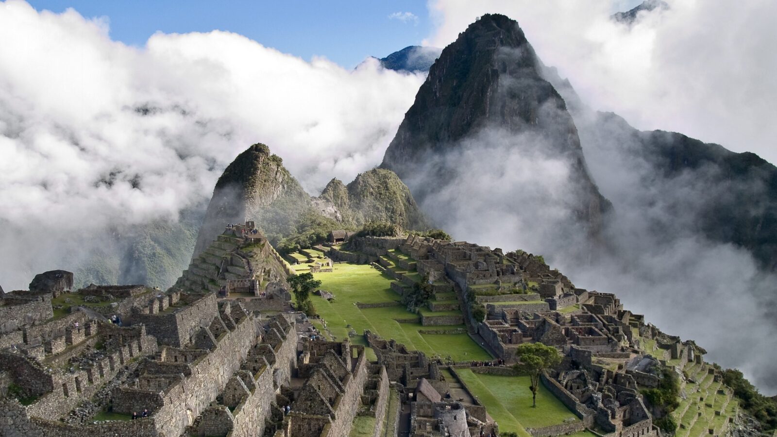 Ancient stone ruins on a green mountain ridge surrounded by clouds for luxury Latin America grand tour vacations.