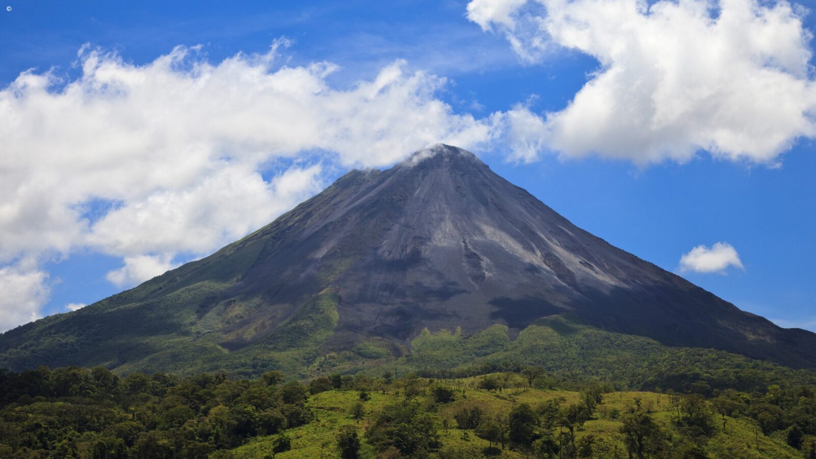 Large conical volcano with a dark peak and green base under a blue sky for luxury Latin America grand tours.