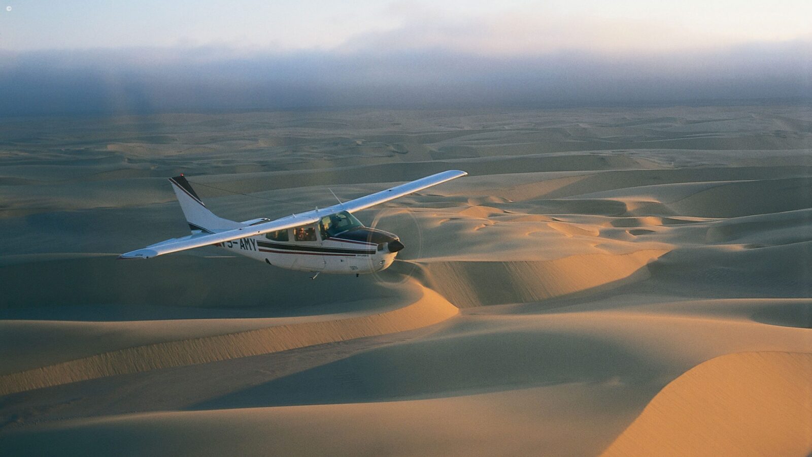 Small white plane with tail number ZS-AMY flying over desert sand dunes on luxury honeymoon grand tours africa.