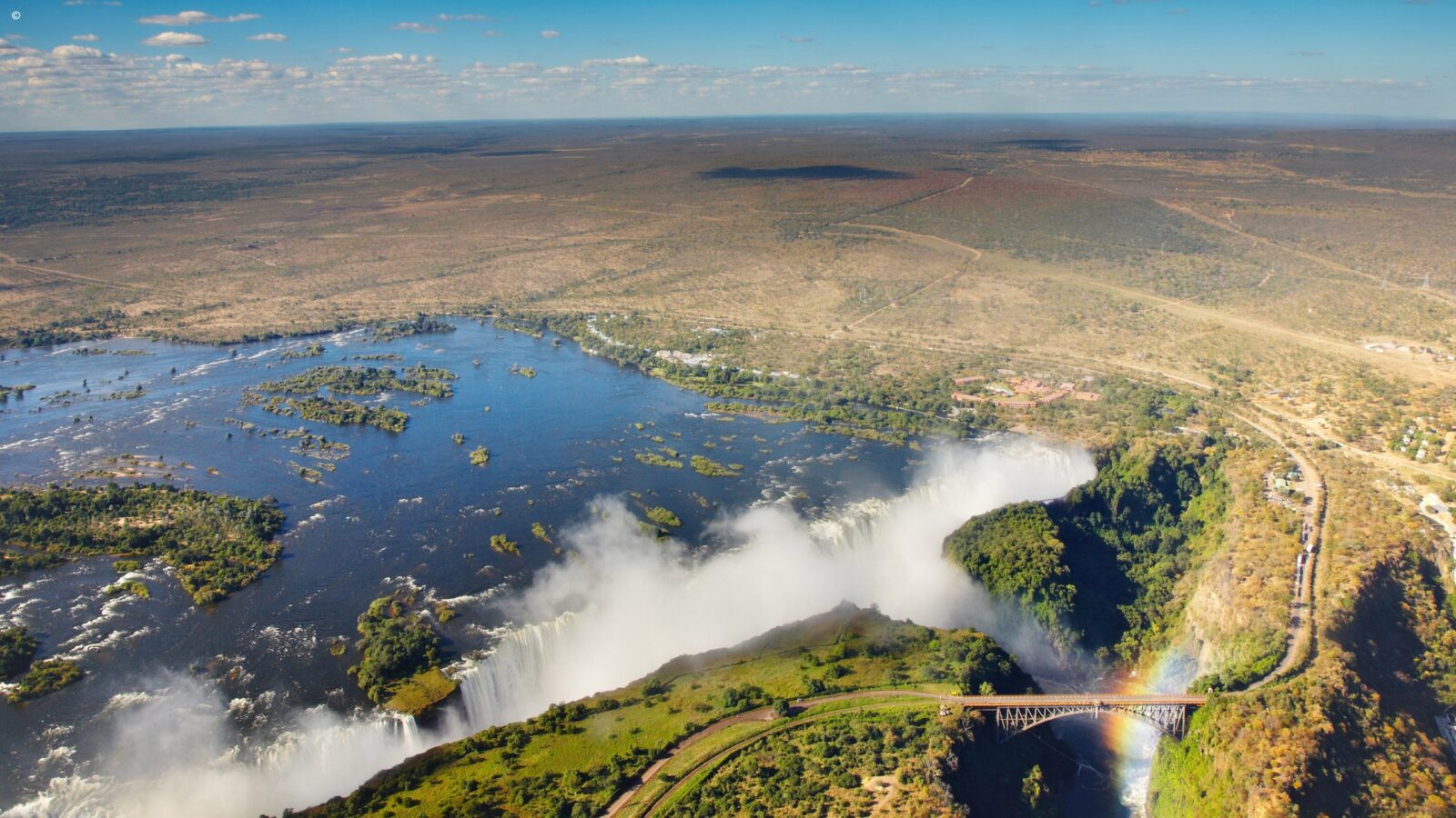 Aerial view of Victoria Falls and a rainbow over the bridge during luxury honeymoon grand tours africa.