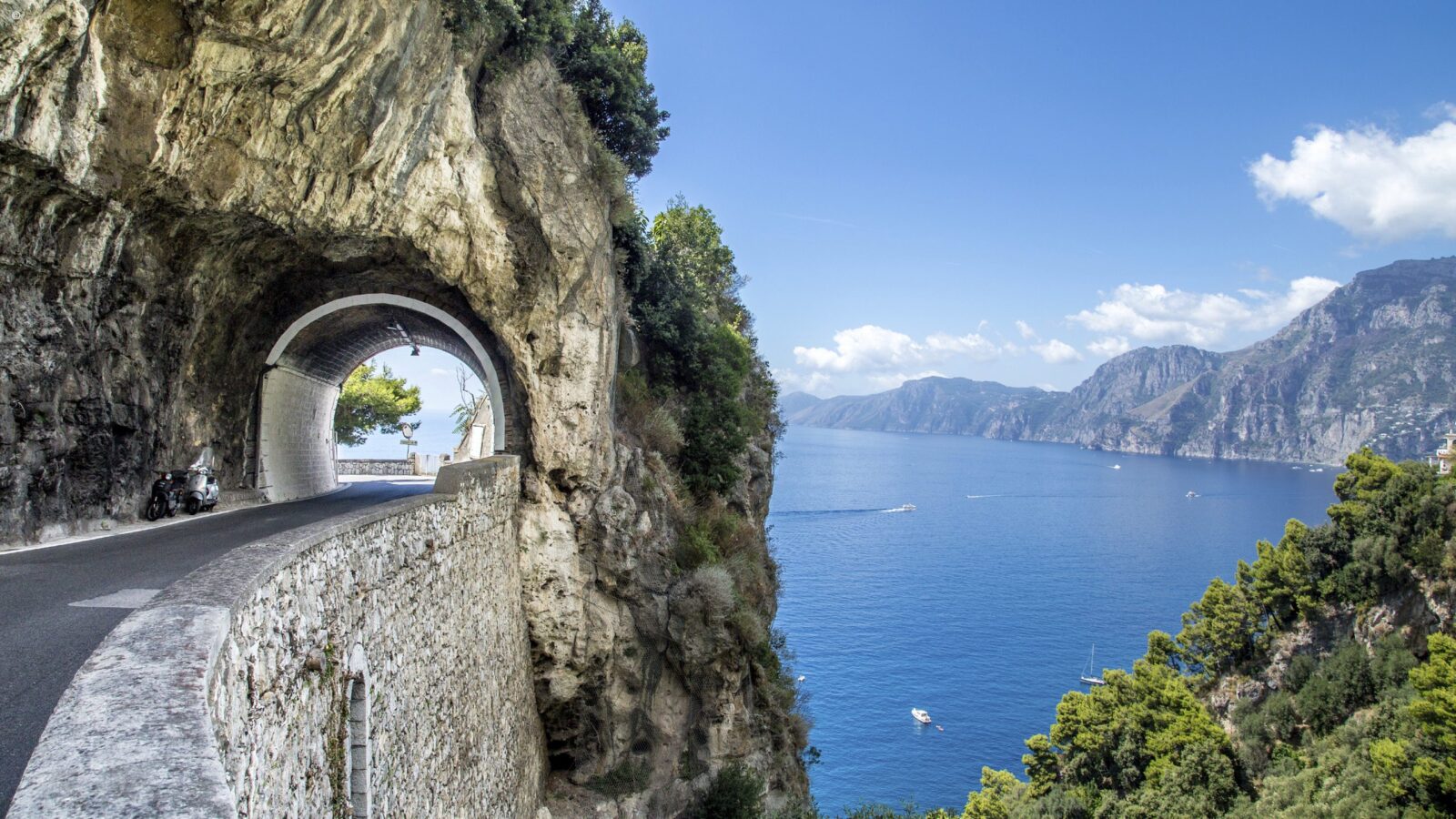 Scenic road through a natural rock tunnel overlooking the sea on luxury Amalfi Coast holidays.
