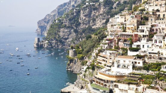 Pastel houses stacked on a steep hillside overlook a sea dotted with white boats on luxury Amalfi Coast trips.