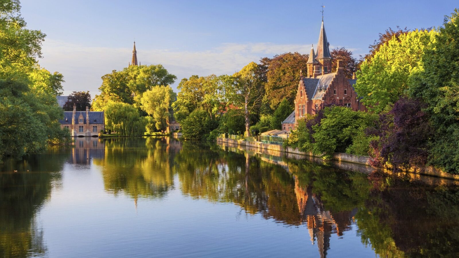 Traditional Dutch-style buildings by a still canal with autumn trees lining the edge of the water
