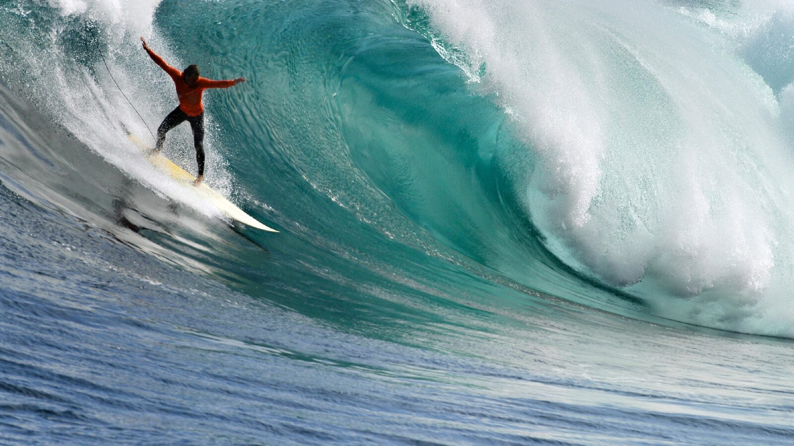 A surfer in an orange shirt riding a giant turquoise wave during luxury Eastern Cape vacations.