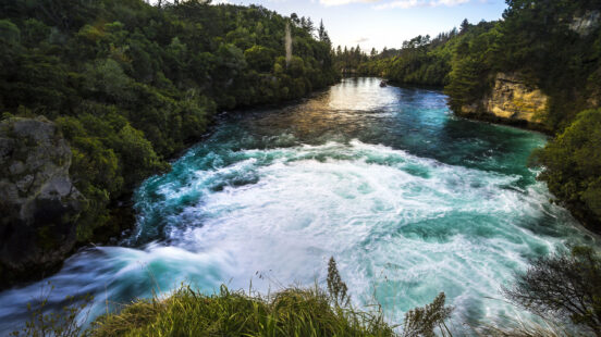 Rushing turquoise river water and white rapids flowing between lush green forested banks.