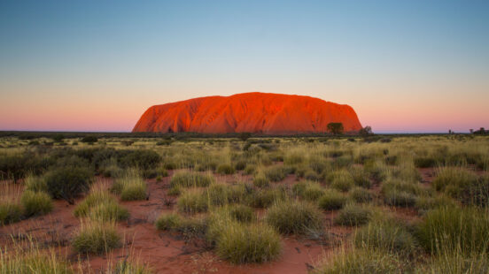 Uluru (Ayers Rock) is an orange-red rock formation in the Australian desert at sunset, a scenic stop on luxury Australia vacations.
