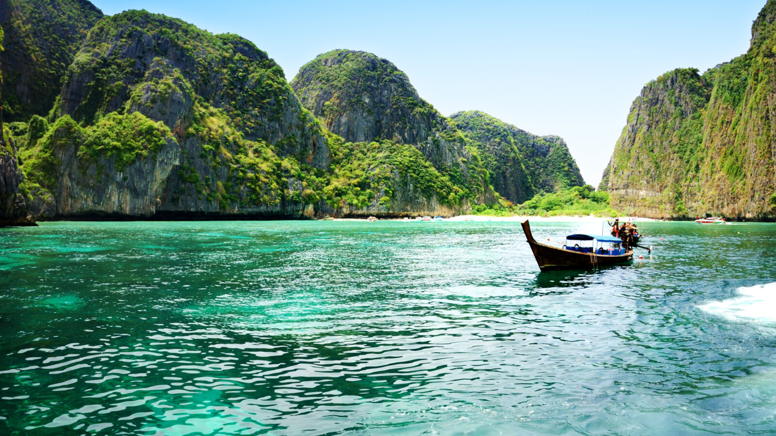 A wooden boat on bright green water surrounded by steep, greenery-covered cliffs in a tropical bay.